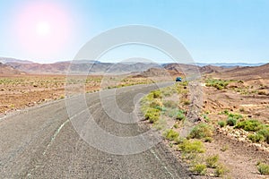 An arid hot desert with mountains and a road under a blue sky