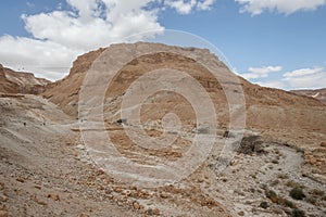 Arid landscape featuring a dry, brown rocky terrain with sparse patches of grass on the ground