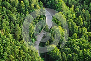 An ariel shot of a curvy narrow road in the middle of the forest surrounded by trees