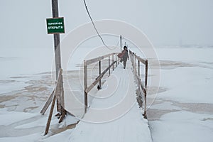 ARKHANGELSK, RUSSIA - JANUARY 06 2022: A girl with a pram crosses an ice-hole on a wooden bridge