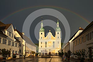 Arlesheim Cathedral after a thunderstorm. The sky is dark with a rainbow, the evening sun is illuminating the cathedral. Arlesheim