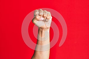 Arm of caucasian white young man over red isolated background doing protest and revolution gesture, fist expressing force and