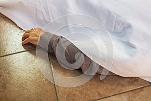 Arm of a deceased woman who comes out of the white sheet used to cover the corpse