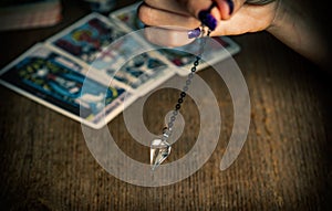 Arm of a dowser with hand-held pendulum on the background of tarot cards.