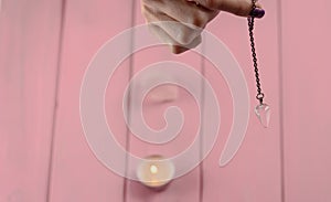 Arm of a dowser with hand-held pendulum on a chain with a natural crystal on a background of pink wood texture photo