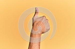 Arm and hand of caucasian man over yellow  background doing successful approval gesture with thumbs up, validation and