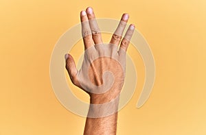Arm and hand of caucasian man over yellow  background greeting doing vulcan salute, showing back of the hand and fingers,