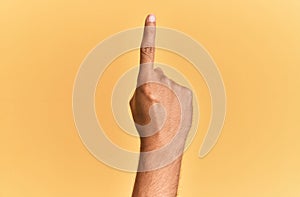 Arm and hand of caucasian man over yellow isolated background counting number one using index finger, showing idea and