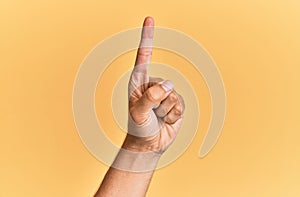 Arm and hand of caucasian man over yellow isolated background counting number one using index finger, showing idea and