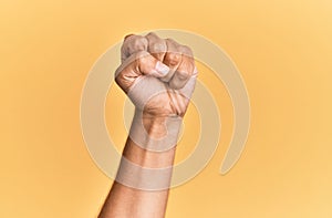 Arm and hand of caucasian man over yellow isolated background doing protest and revolution gesture, fist expressing force and
