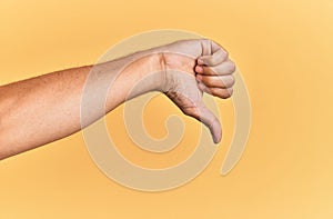 Arm and hand of caucasian man over yellow isolated background doing thumbs down rejection gesture, disapproval dislike and