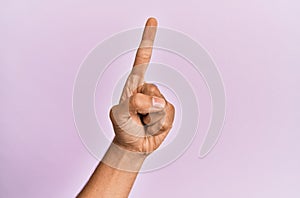 Arm and hand of caucasian young man over pink  background counting number one using index finger, showing idea and