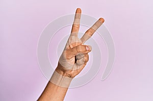 Arm and hand of caucasian young man over pink isolated background counting number 2 showing two fingers, gesturing victory and