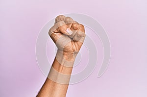 Arm and hand of caucasian young man over pink isolated background doing protest and revolution gesture, fist expressing force and