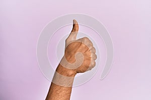 Arm and hand of caucasian young man over pink isolated background doing successful approval gesture with thumbs up, validation and