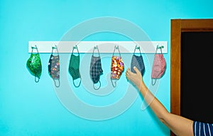 Arm of a person picking up a hygienic mask. Anti-Covid-19 masks hanging from a coat rack. New normal concept