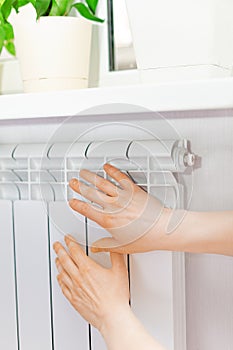 Arm put on heating white radiator.Windowsill with flowers.