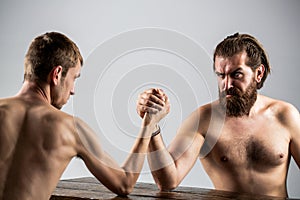 Arm wrestling. Heavily muscled bearded man arm wrestling a puny weak man. Arms wrestling thin hand, big strong arm in