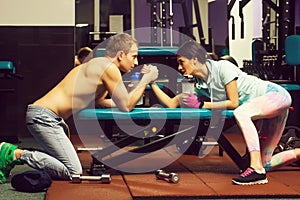 Arm wrestling muscular man and girl at gym