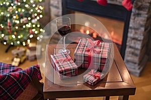 Armchair with plaid, packing gift boxes for family and glass of wine near christmas tree and fireplace. Top view.