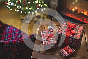 Armchair with plaid, packing gift boxes for family and glass of wine near christmas tree and fireplace. Top view.