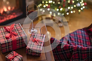 Armchair with plaid, packing gift boxes for family and glass of wine near christmas tree and fireplace. Top view.
