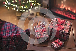 Armchair with plaid, packing gift boxes for family and glass of wine near christmas tree and fireplace. Top view