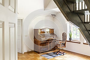 Armchair on rug next to wooden piano in white living room interior with plant and stairs. Real photo