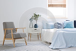 Armchair standing on striped carpet in white bedroom interior wi