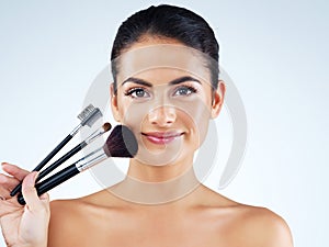 Armed with all the beauty tools I need. Studio portrait of an attractive young woman holding makeup brushes against a