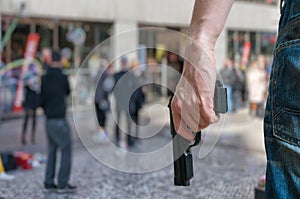 Armed man (attacker) holds pistol in public place. Many people on street. photo