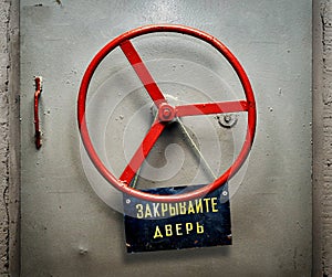 Armored bunker door with hanging shabby signboard with russian CLOSE THE DOOR warning