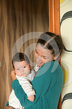 In the arms of a cheerful mom. Portrait of charming toddler with blue eyes and chubby cheeks resting vertically in his mother`s