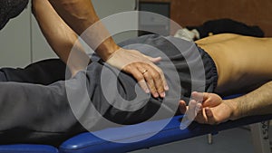 Arms of massagist doing healing rubdown of hip to young athlete lying on massage table. Male hands of masseur massaging