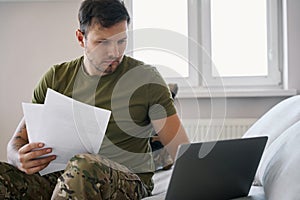 Army combatant holding documentation while starting at laptop screen