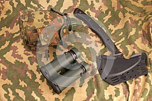 army flask, tactical tomahawk ax, binoculars. Military kit, ammunition laid out on a camouflage background
