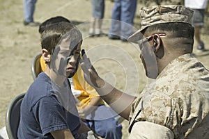 Army solider applying camouflage to young boy