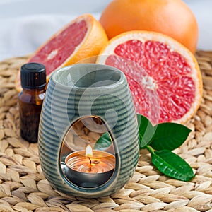 Aroma lamp with grapefruit essential oil on woven mat, grapefruits on background, square format