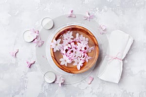 Aromatherapy, beauty and spa background with perfumed pink flowers water in wooden bowl and candles on stone table. Flat lay.