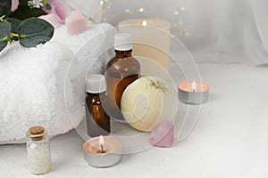 Aromatherapy concept with essential oil bottle, bath bomb, burning candles on light background.