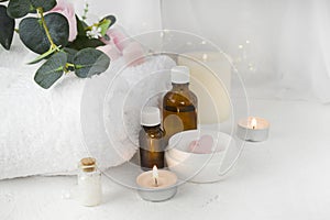 Aromatherapy concept with essential oil bottle, body care cream, burning candles on light background.