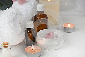 Aromatherapy concept with essential oil bottle, body care cream, burning candles on light background.