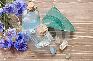Aromatherapy or cosmetic concept. Cornflower flower, water in glass bottle and natural minerals stones on wooden brown background