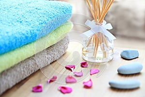 Aromatherapy reed difuser bottle on a wooden table with towels, petals and massage stones