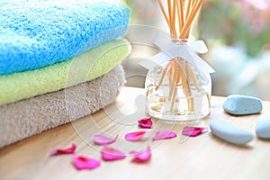 Aromatherapy reed difuser bottle on a wooden table with towels, petals and massage stones