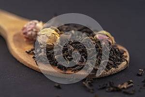 aromatic black dry tea with rose flowers on a wooden spoon isolated on black background .