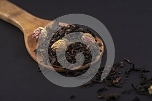 aromatic black dry tea with rose flowers on a wooden spoon isolated on black background .