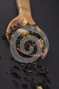 aromatic black dry tea with rose flowers on a wooden spoon isolated on black background .