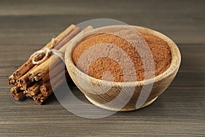 Aromatic cinnamon powder in bowl and sticks on wooden table