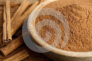 Aromatic cinnamon powder in bowl and sticks on wooden table, closeup